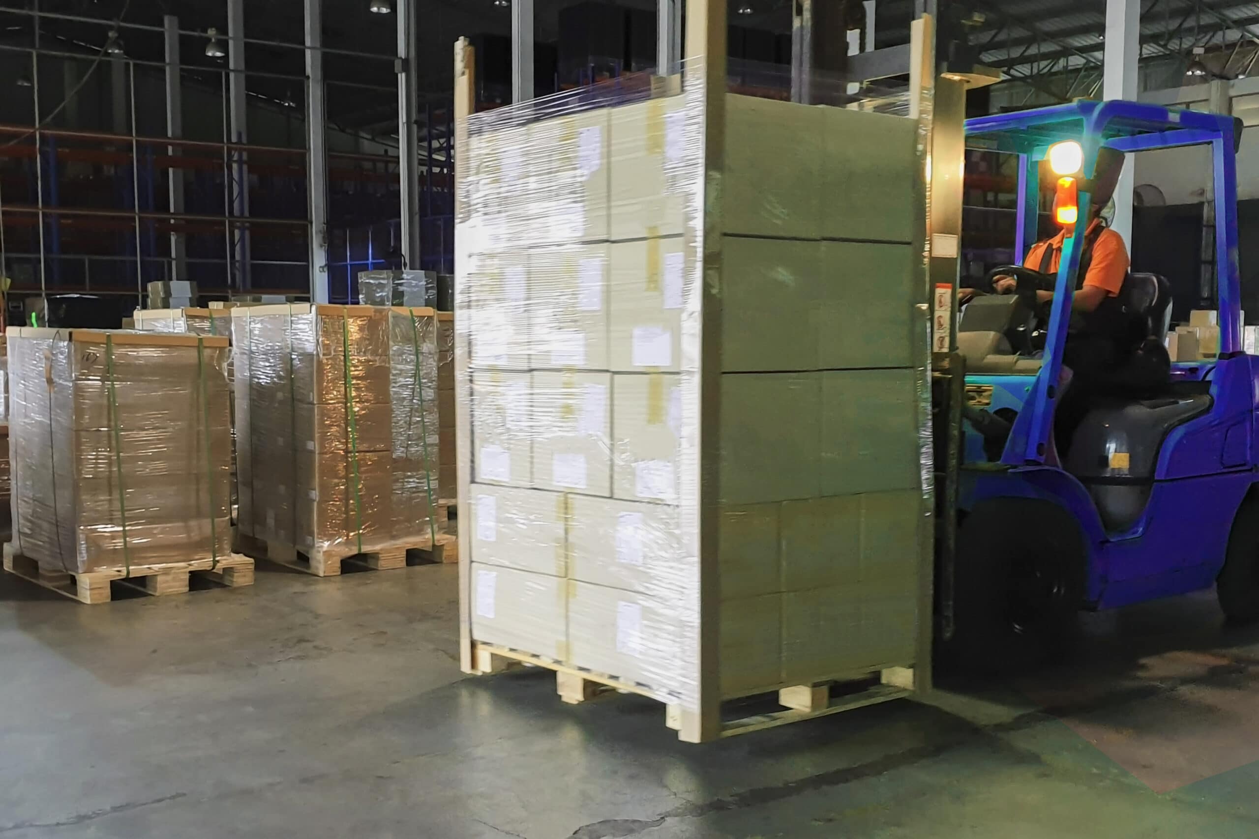 Forklift driver unloading cargo shipment pallet at warehouse